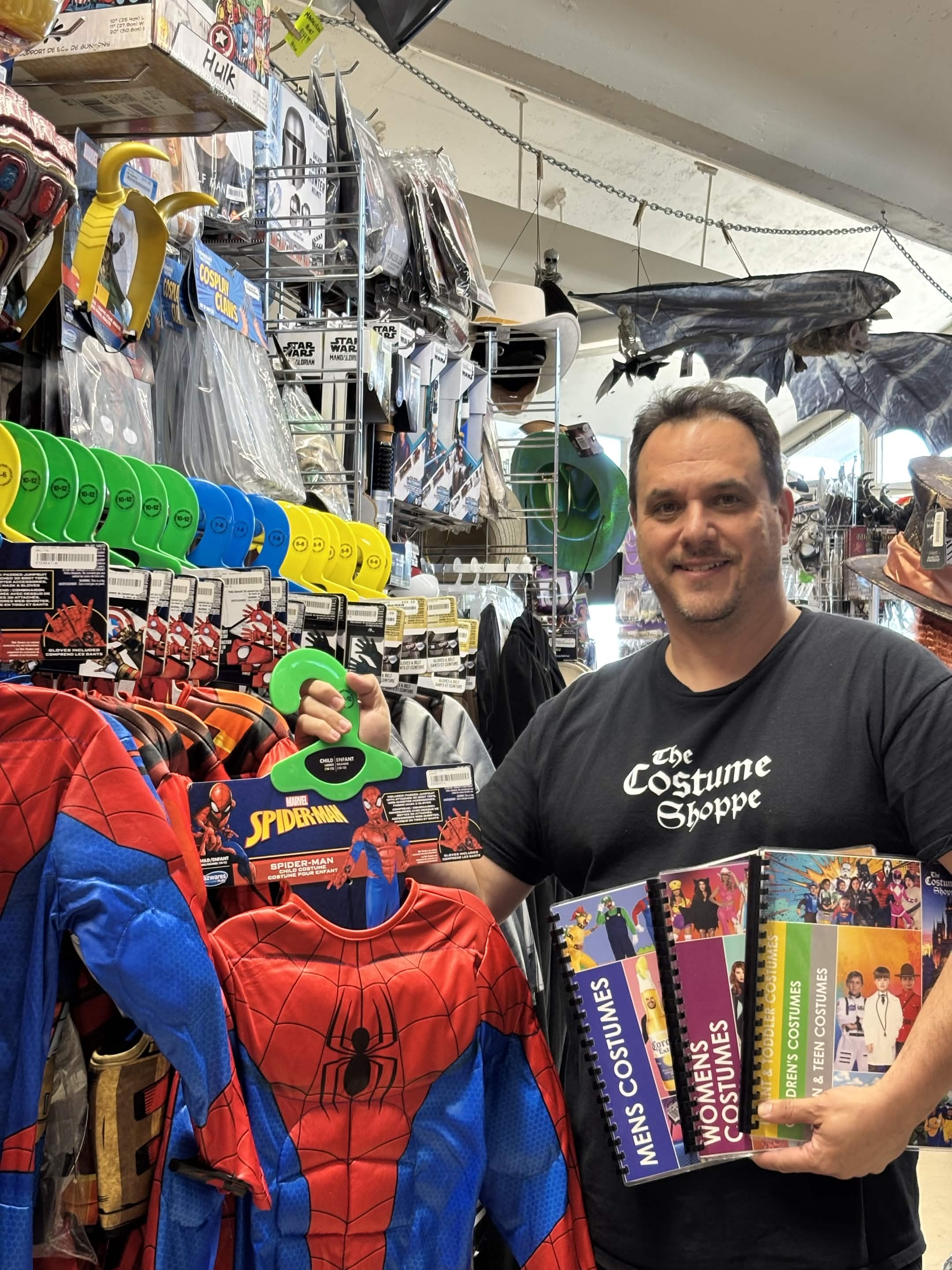 Ry, The Costume Shoppe Guy, with a Spider-Man costume and the store's costume catalogs featuring over 1,200 styles, Calgary Alberta